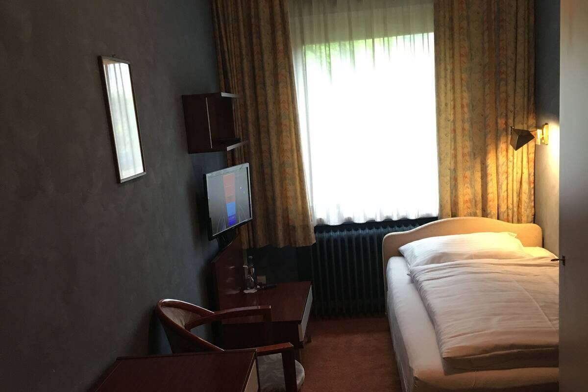 Une chambre d’hôtel comprenant un lit, un bureau avec une chaise, une télévision et une fenêtre avec des rideaux.