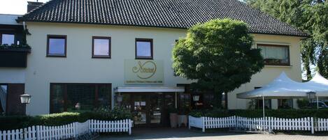 A building with a tiled roof, a sign with a logo and text, a white picket fence, and a tree in front.