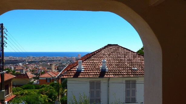 A view through an archway of a coastal city with terracotta-roofed buildings and a clear blue sky. - Villa Bennecourt (Nice)