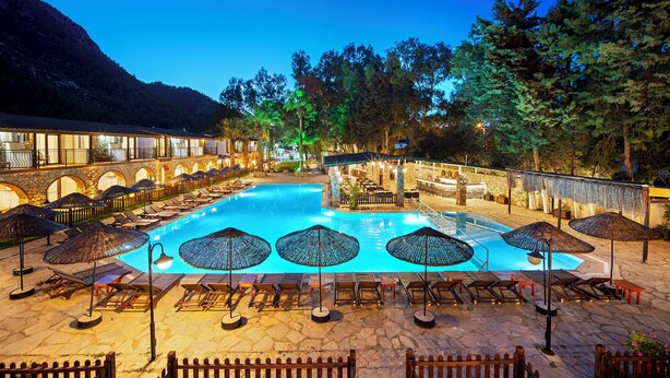 A swimming pool with lounge chairs and umbrellas, surrounded by a stone patio and a bar area. - Alados Otel (Marmaris)