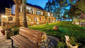 A stone building with a balcony, a wooden bench, and a well-maintained garden. - Alados Otel (Marmaris)