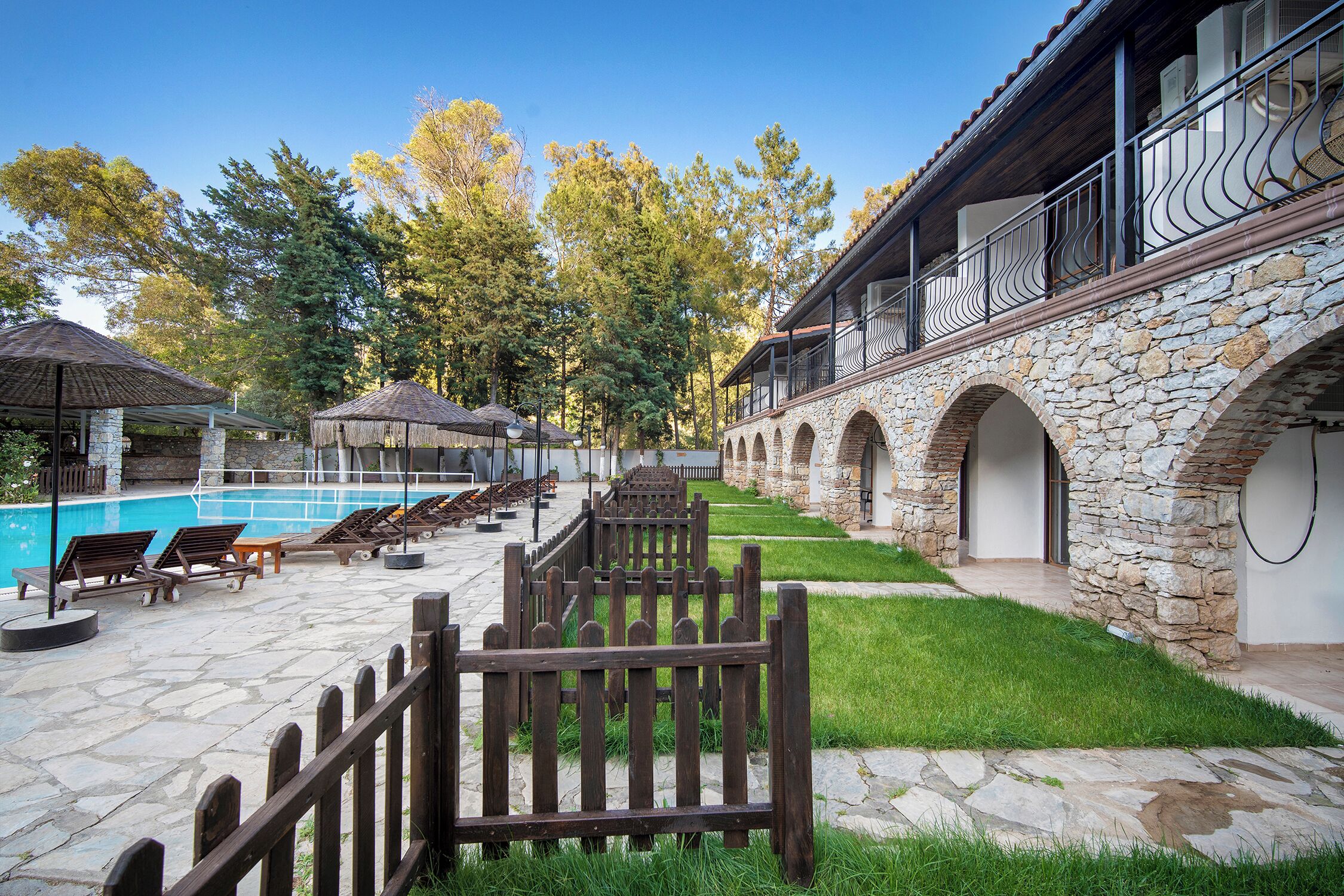 A poolside area with lounge chairs, a stone wall, and a wooden fence.