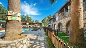 A pathway lined with trees and a wooden fence leading to a building with stone arches and a balcony. - Alados Otel (Marmaris)