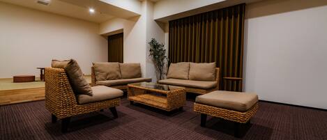 A modern living room with three wicker sofas and a coffee table, a wooden floor, and a large window with curtains.