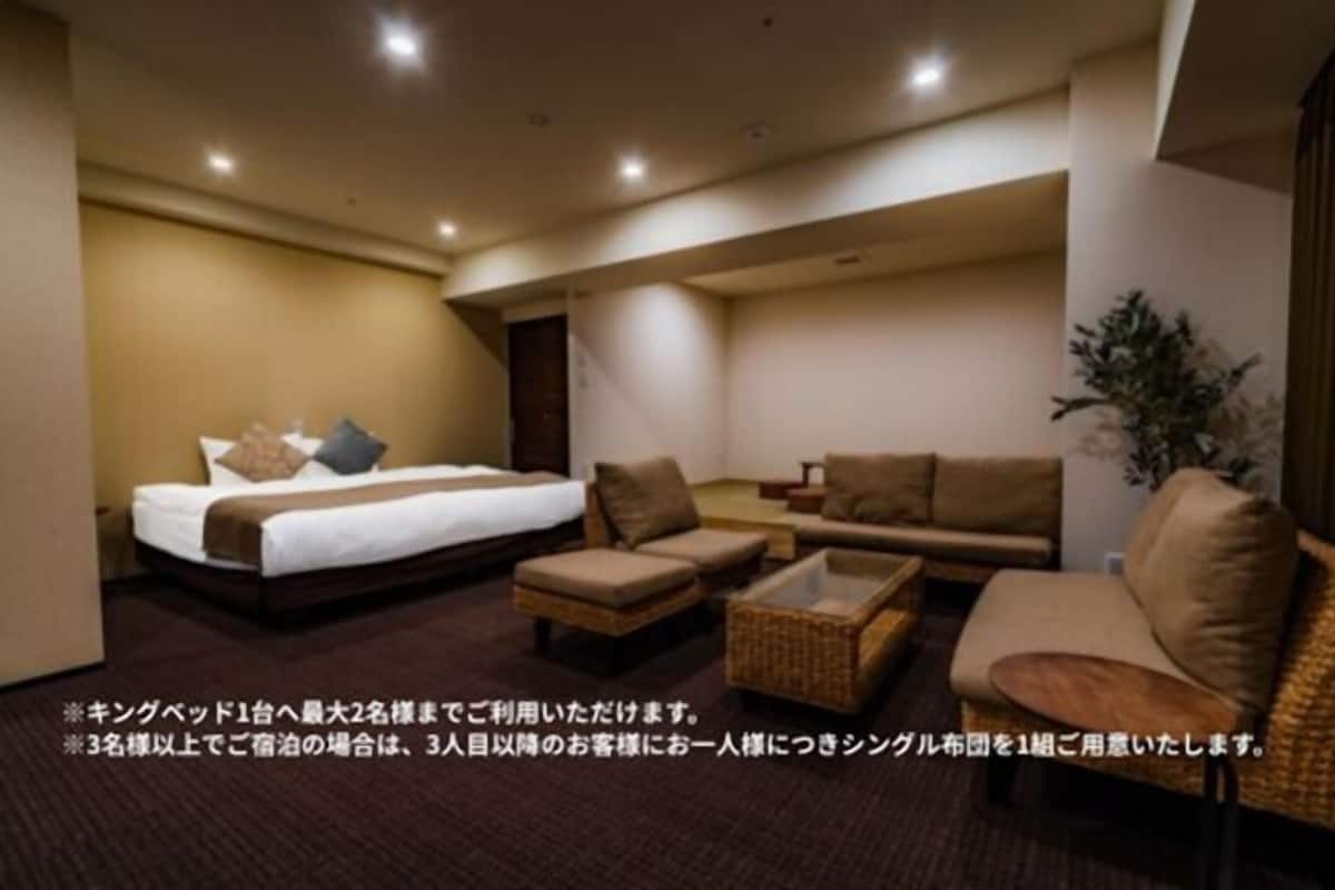A hotel room with a bed, two sofas, a small table, and a potted plant.