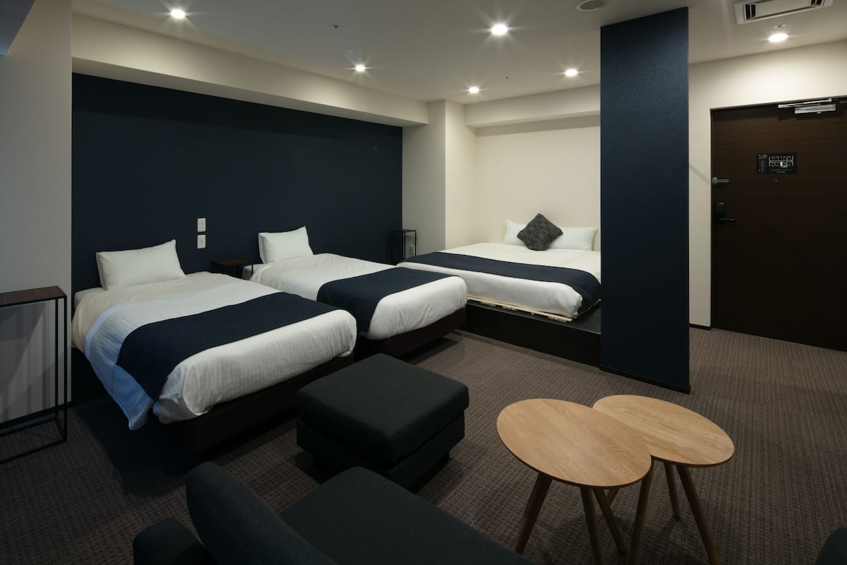 A hotel room with two beds, a small seating area, and a door with a control panel.