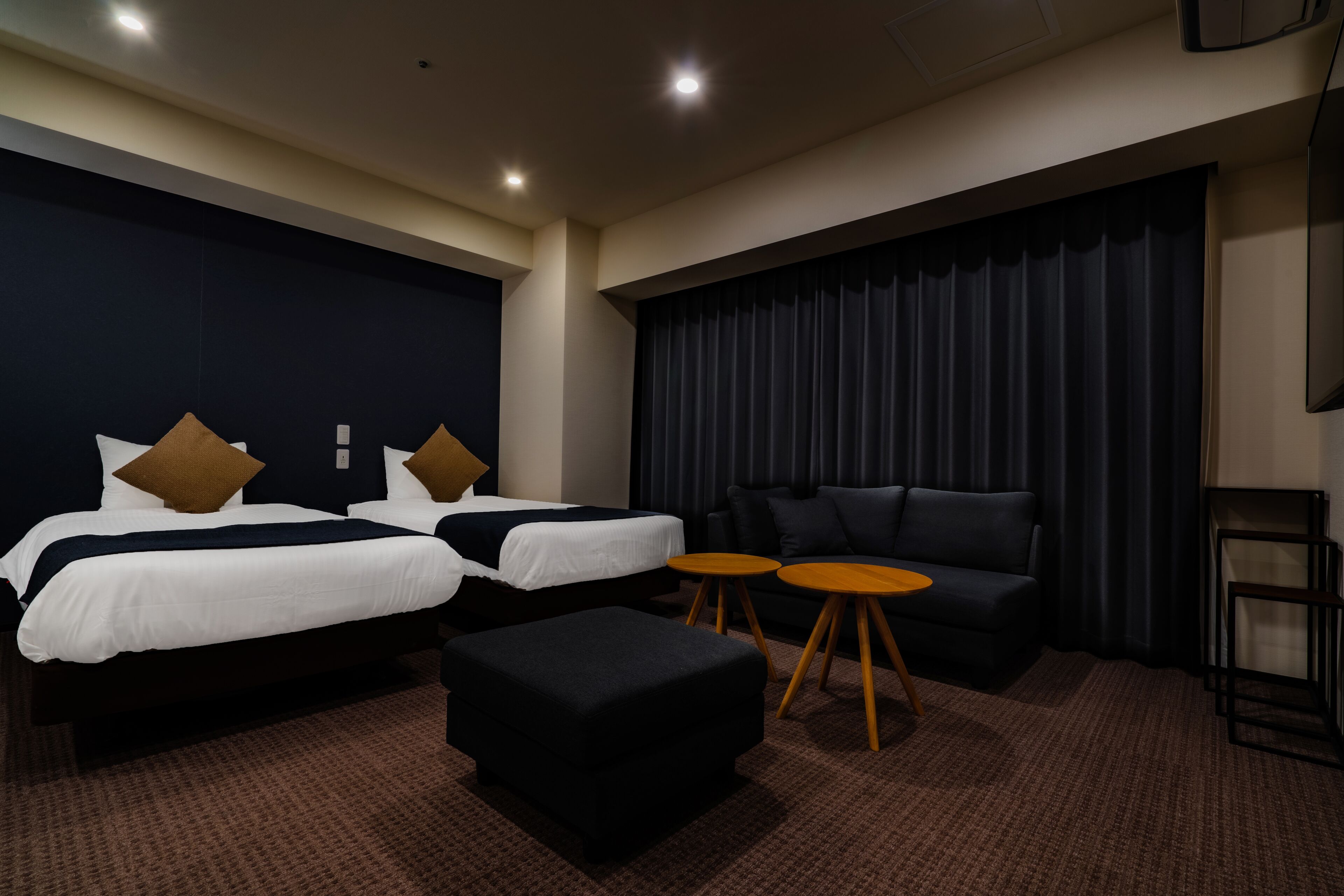 A hotel room with two beds, a sofa, two small round tables, and a large window with curtains.