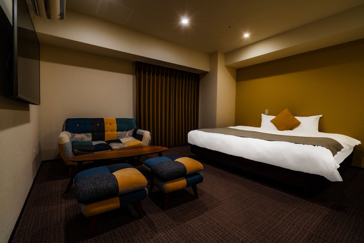 A hotel room with a bed, a sofa, and two ottomans.