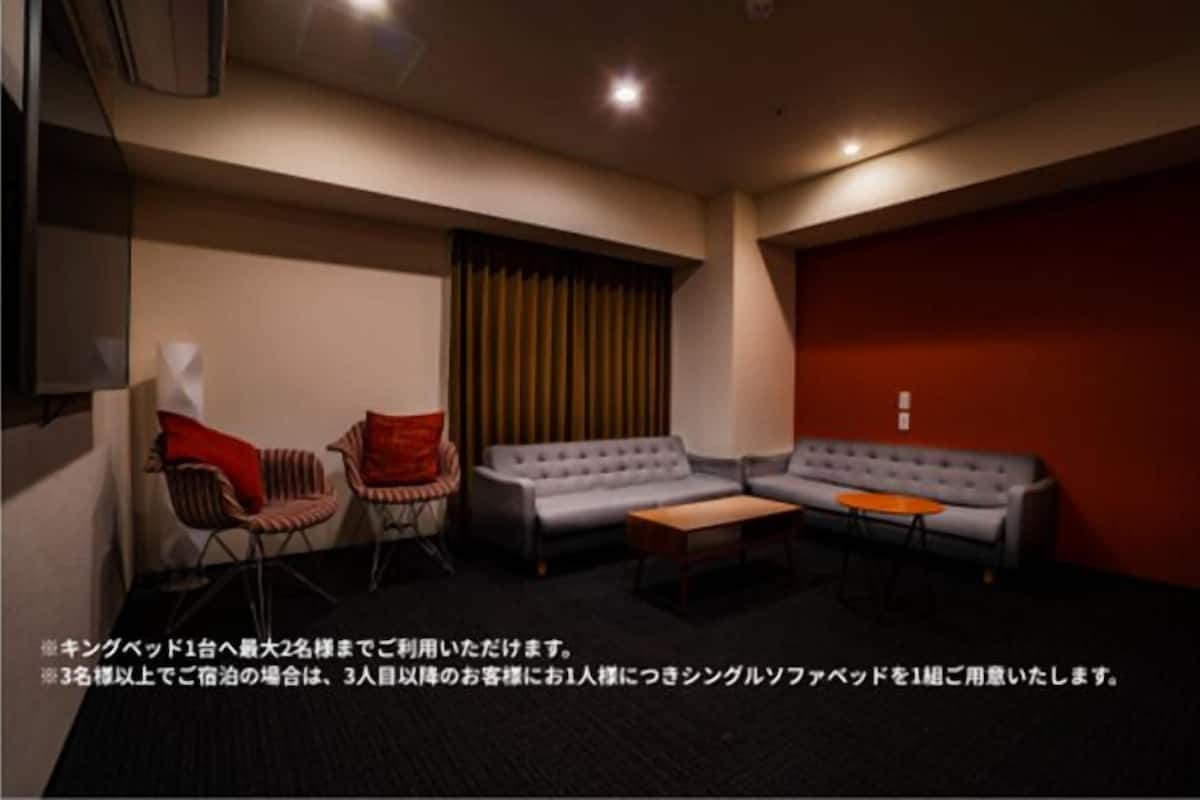 A room with a grey sofa, two armchairs, a small table, and a red accent wall.