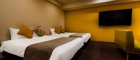 A hotel room with two beds, a flat-screen TV, and a green armchair.