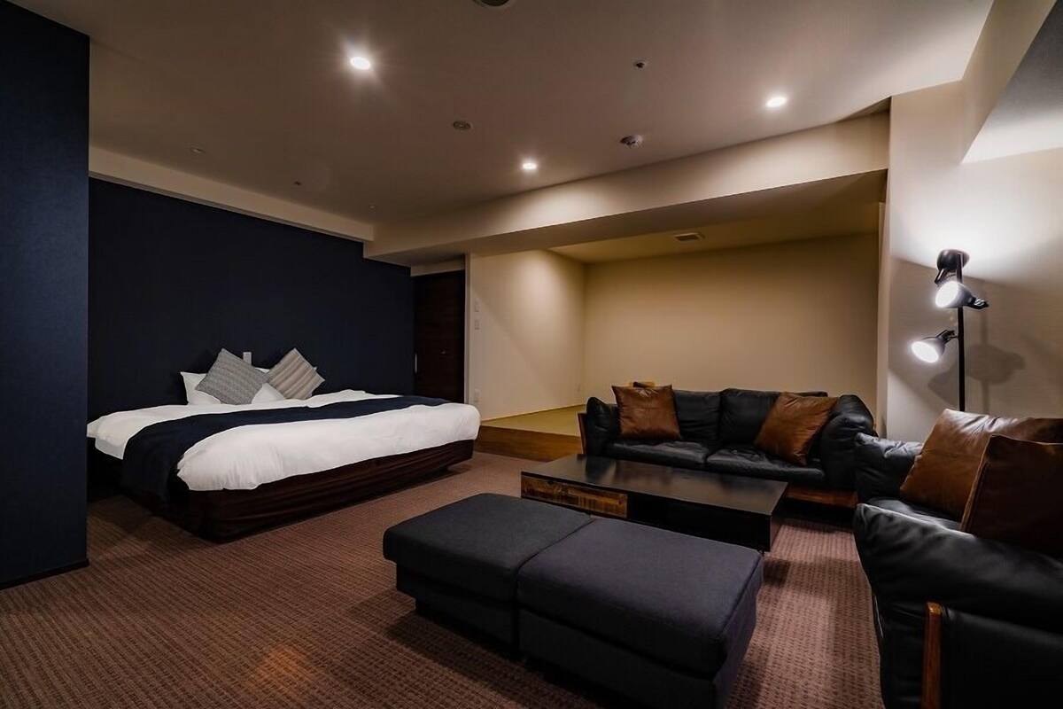 A modern hotel room with a bed, a sofa, a coffee table, and a desk.