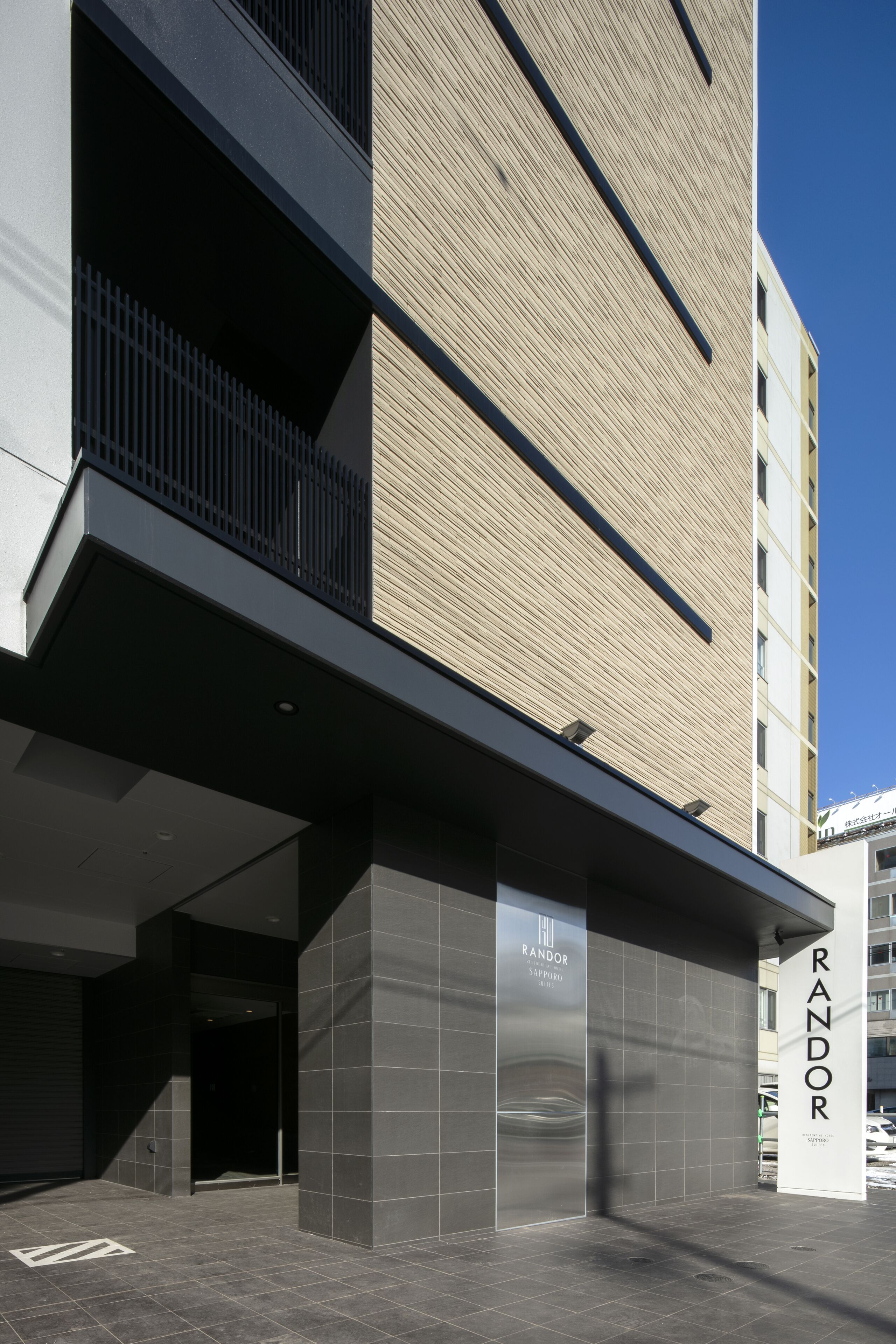 Een modern gebouw met een opvallend “RANDOR” bord, met een strakke, geometrische gevel en een heldere lucht op de achtergrond.