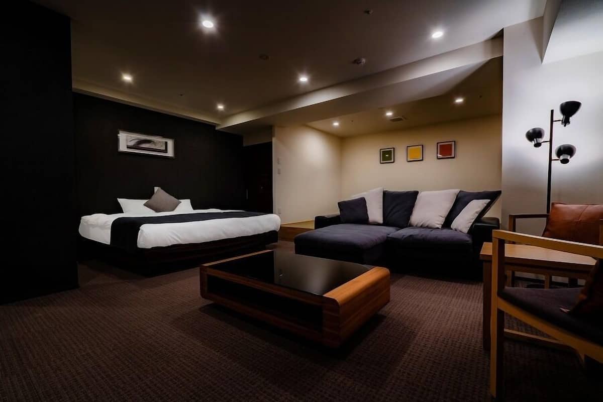 A modern hotel room with a bed, a sofa, a coffee table, and a chair.