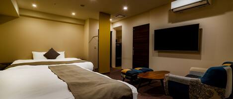 A hotel room with a large bed, a sofa, a small table, and an air conditioning unit.