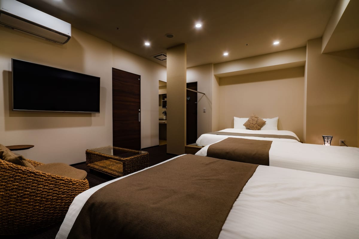 A hotel room with two beds, a flat-screen TV, a wicker chair, and a wardrobe.