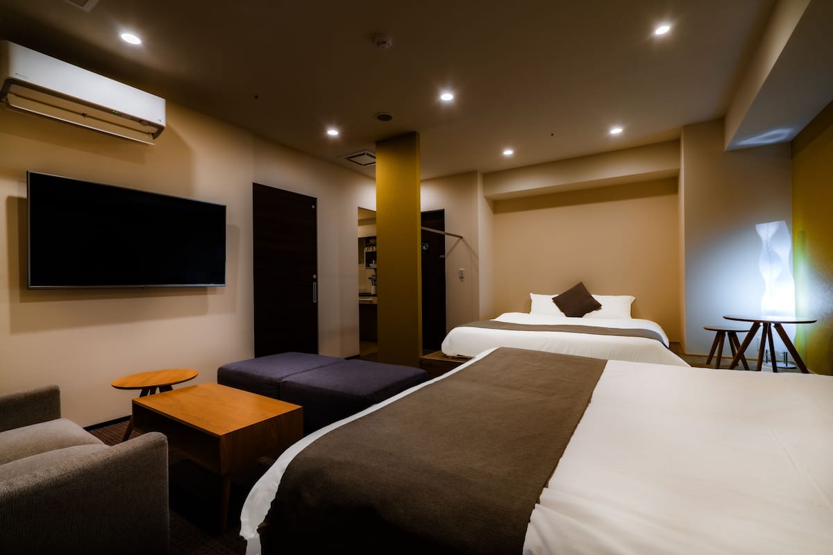 A hotel room with two beds, a TV, a small table, and a seating area.