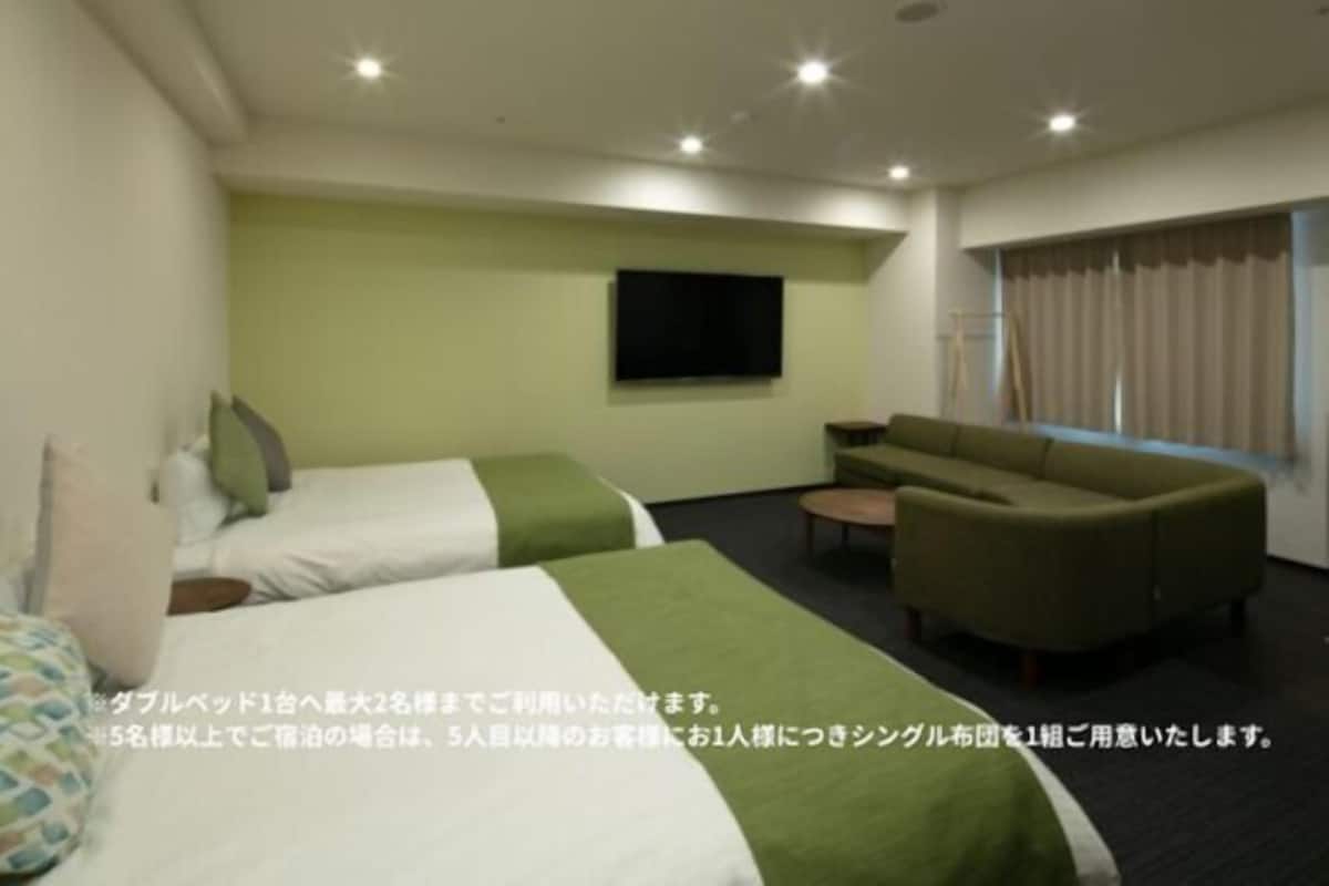 A hotel room with two beds, a sofa, a TV, and a window with curtains.
