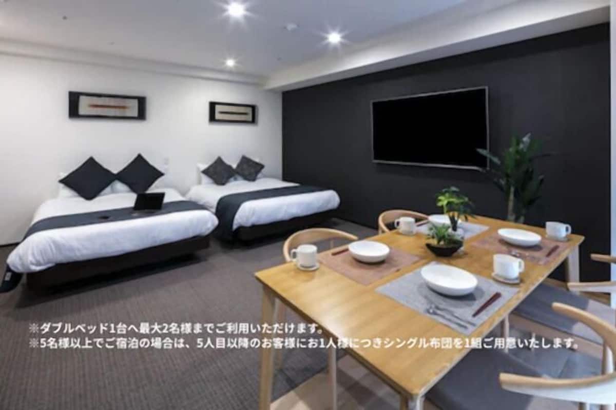 A hotel room with two single beds, a dining table with chairs, and a TV mounted on the wall.