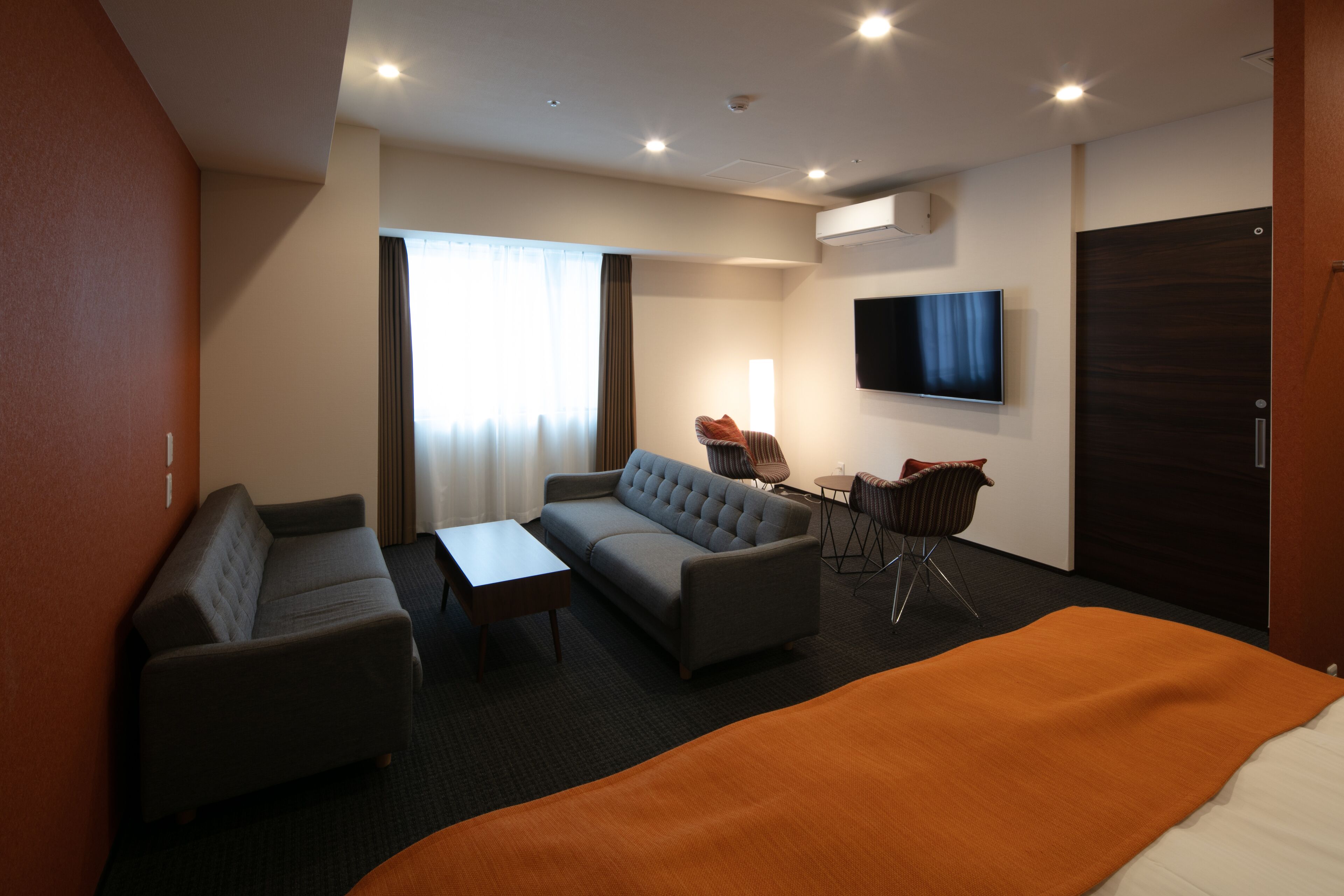 A modern hotel room with a sofa, a small table, a TV, and a large bed.