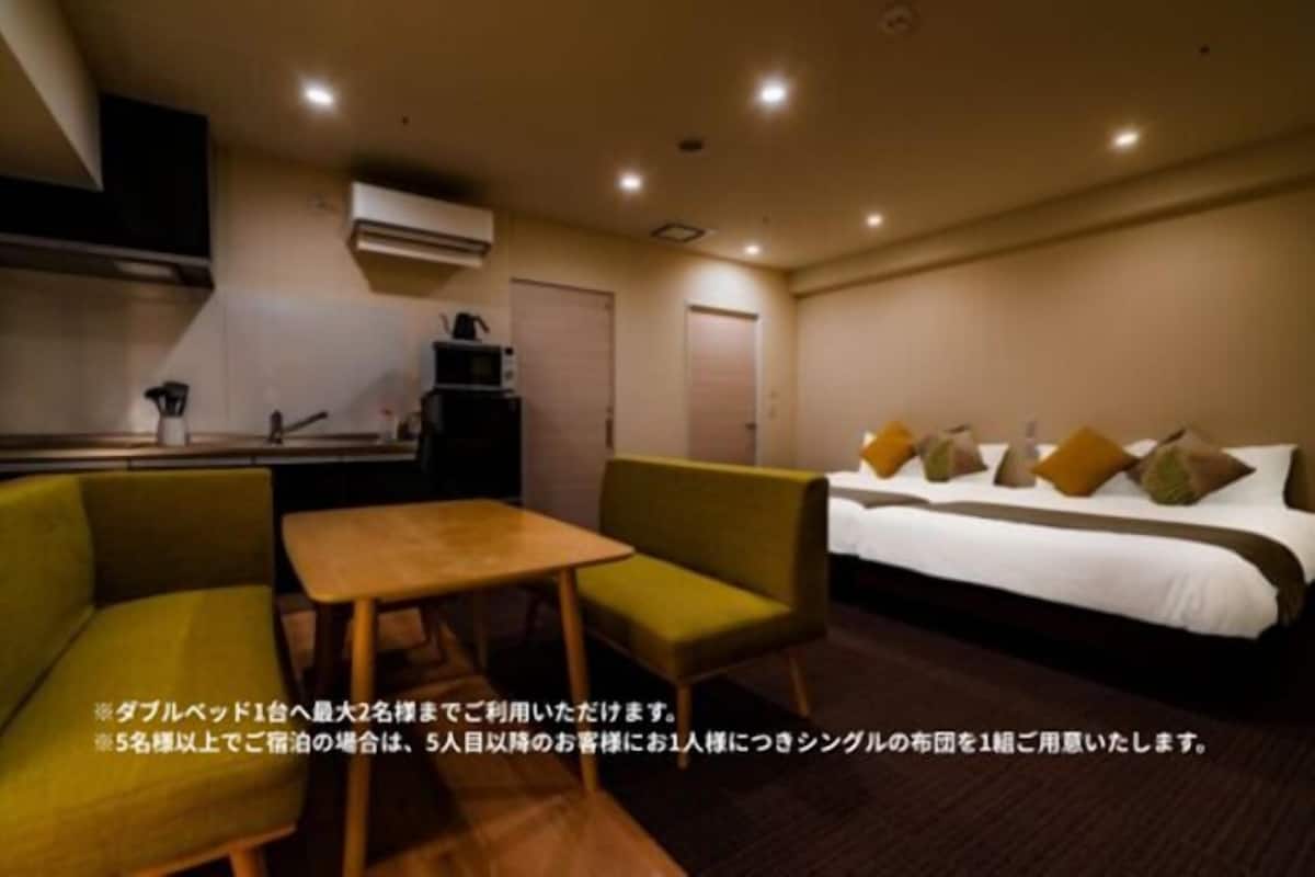 A hotel room with a bed, a small table, two chairs, and a kitchenette.
