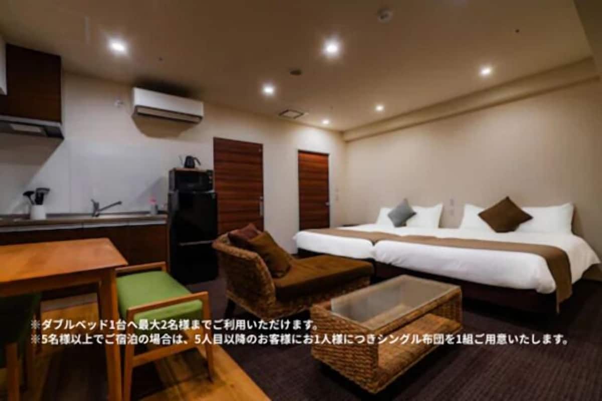A hotel room with a bed, a sofa, a small table, and a kitchenette.