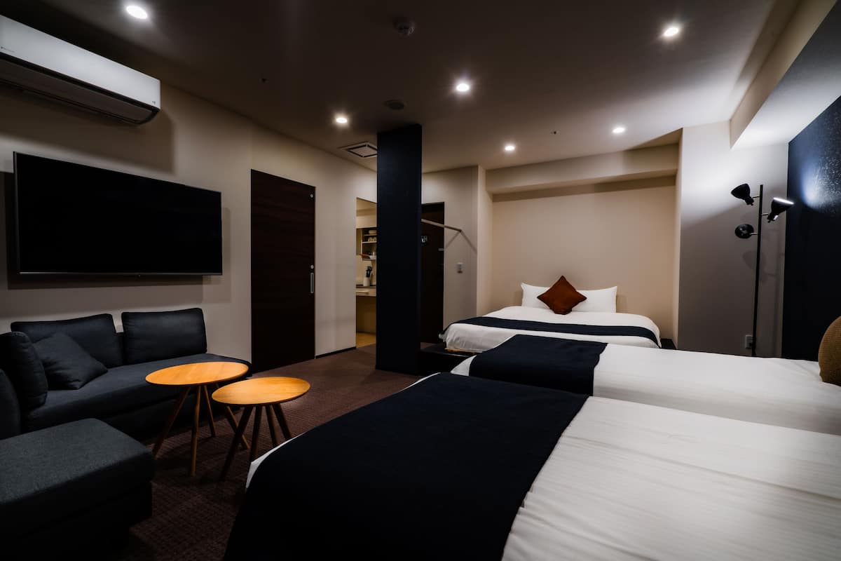 A hotel room with two beds, a sofa, a small table, and a TV.