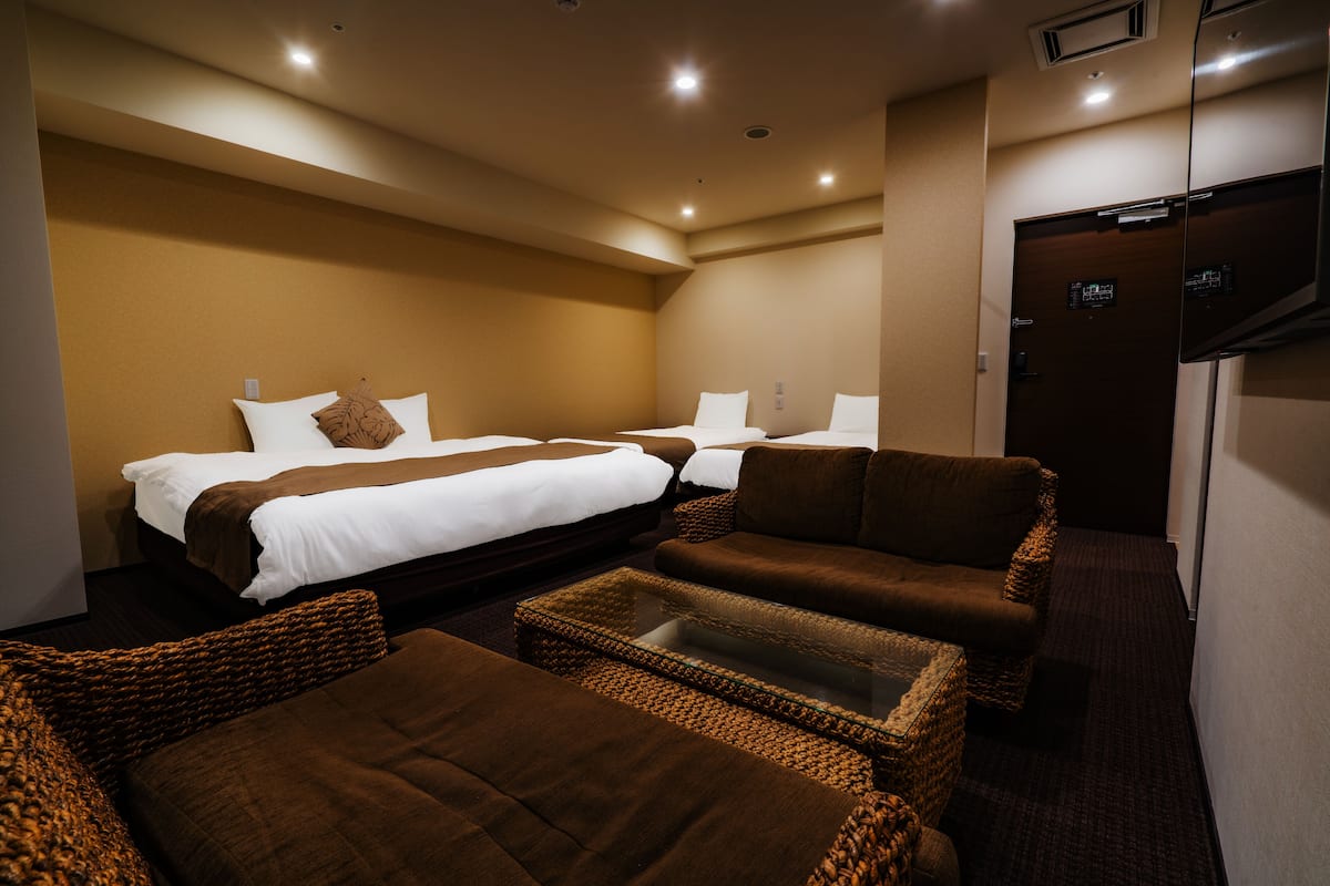 A hotel room with two beds, a sofa, a coffee table, and a television.