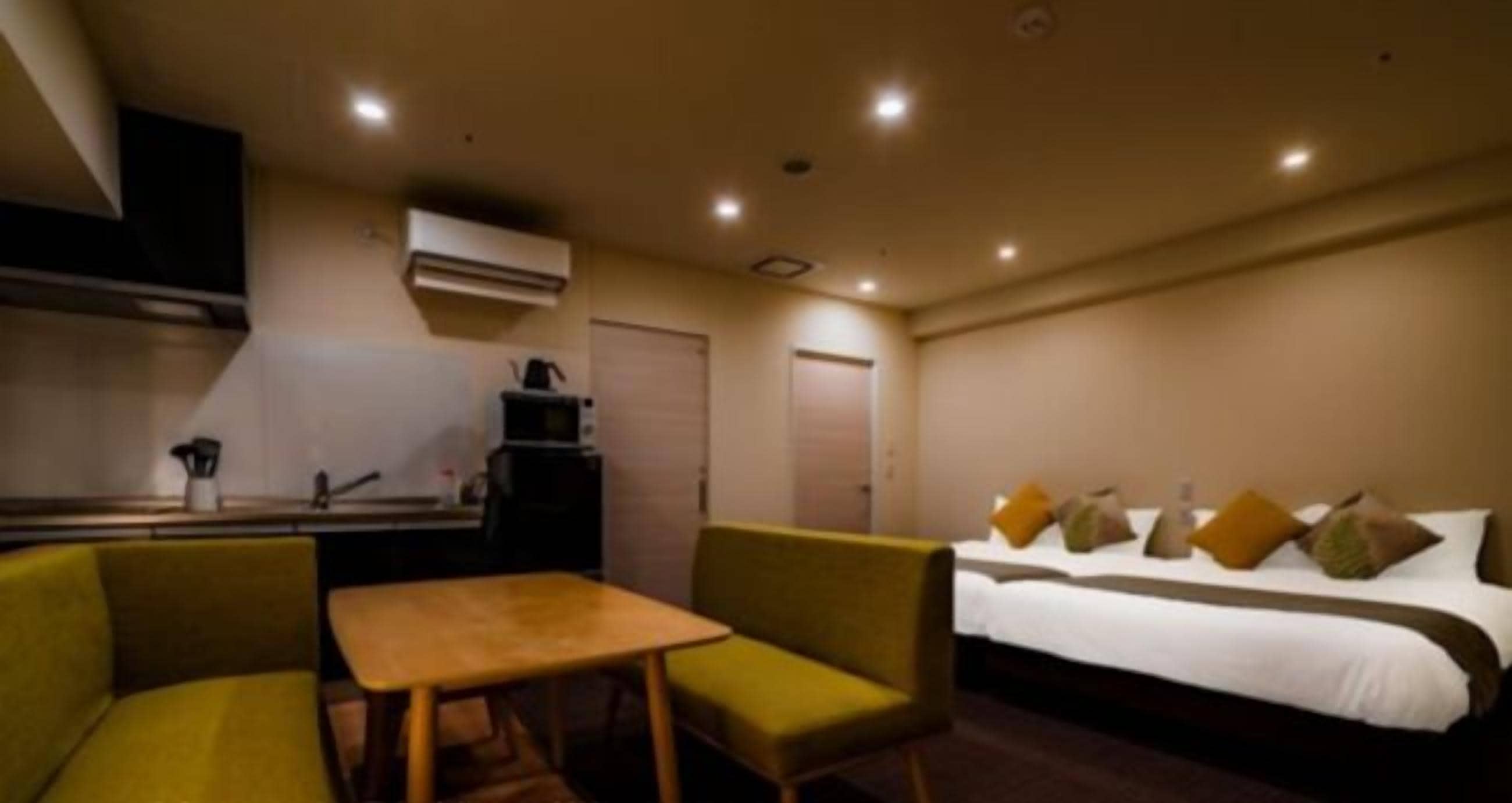 A hotel room with a bed, a small table, two chairs, and a kitchenette.