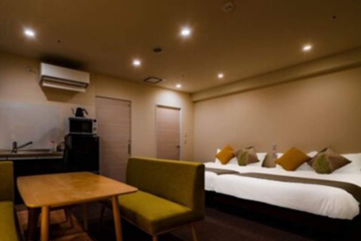Una habitación de hotel con cama, una mesita, dos sillas y una kitchenette.