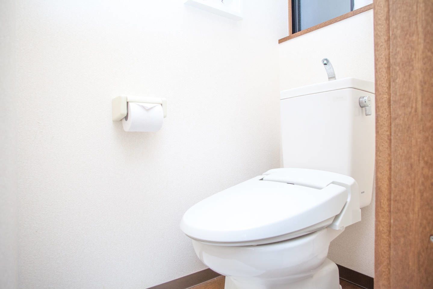 A small, clean bathroom with a white toilet, a toilet paper holder, and a visible water tank.