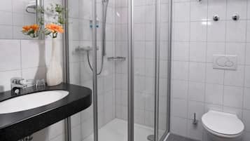 Uma casa de banho moderna com chuveiro envolto em vidro, sanita branca e lavatório preto com um vaso de flores.