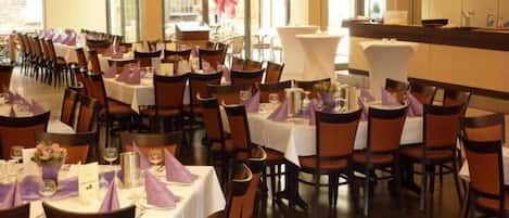A restaurant with multiple tables and chairs, each set with white tablecloths and purple napkins.