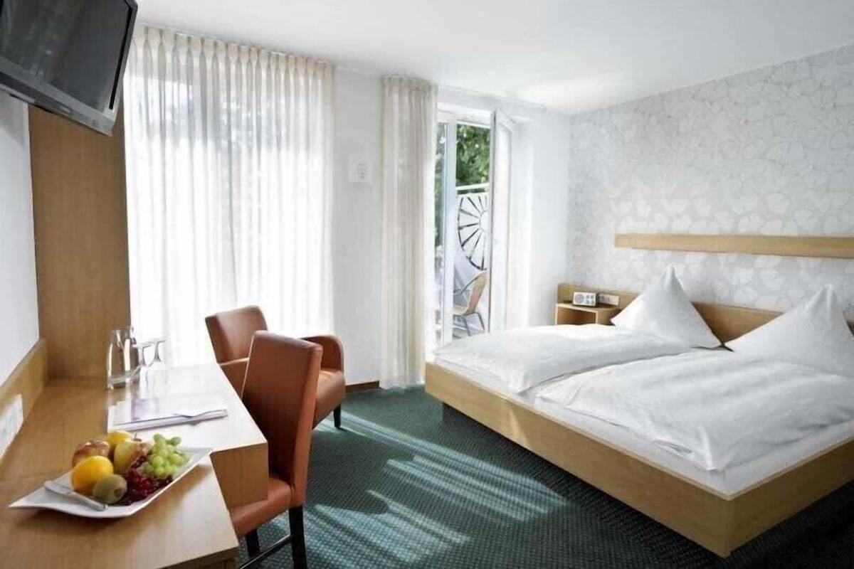 Quarto de hotel com cama, escrivaninha com prato de frutas, cadeira e televisão.