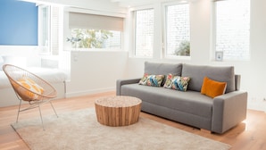 A modern living room with a grey sofa, colorful cushions, a wooden coffee table, and a wicker chair. - La Maison des Arts (Honfleur)