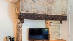 A fireplace with a TV placed below it, a coffee maker, and a tray with cups on a wooden shelf. - La Maison des Arts (Honfleur)