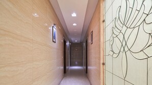 Un pasillo con paredes de mármol, cuadros enmarcados y un panel de vidrio decorativo a la derecha.