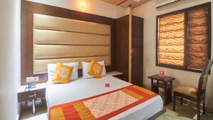 Una habitación de hotel con cama, mesita de noche, silla y ventana con cortinas.
