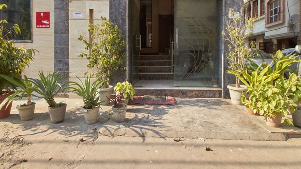 Entrada de un edificio con un letrero de 'No Estacionar', plantas en macetas y un puerta de vidrio que da a una escalera.