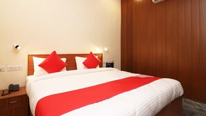 Een netjes opgemaakt bed met witte beddengoed en rode accenten, een houten hoofdbord en een airconditioner aan de muur.