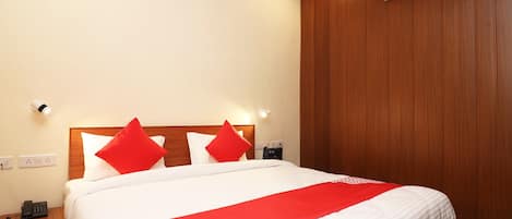 A neatly made bed with white bedding and red accents, a wooden headboard, and an air conditioning unit on the wall.