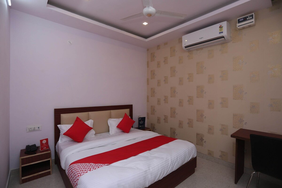 A hotel room with a bed, a nightstand, a desk, an air conditioner, and a ceiling fan.