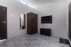 A room with a wooden wardrobe, a flat-screen TV, a small black cabinet, and a marble-patterned floor. - OYO 19292 55 Pillars House (Shillong)