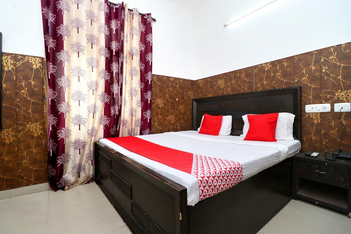 A neatly made bed with red and white bedding, a dark headboard, and a bedside table with a phone and charger.