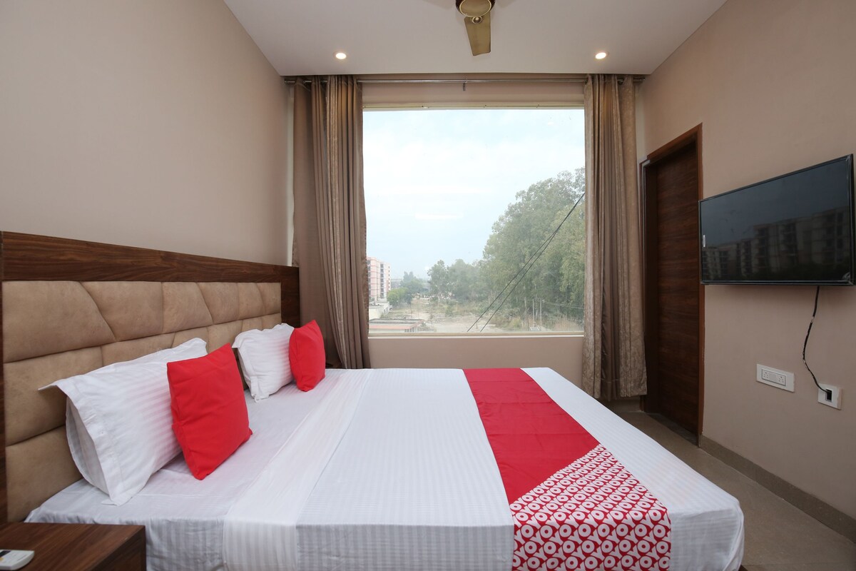 A hotel room with a large bed, a flat-screen TV mounted on the wall, and a window with curtains.