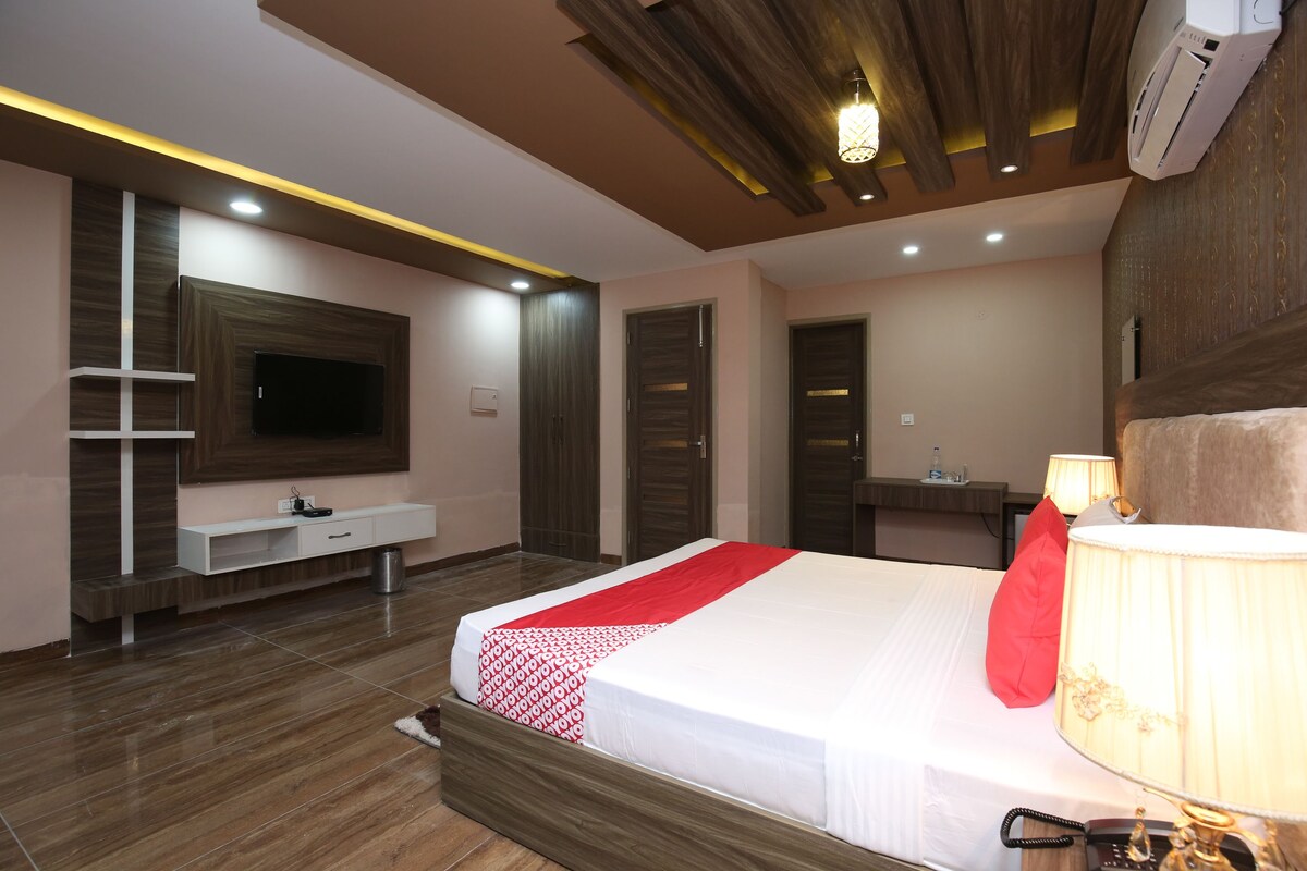 A modern hotel room with a large bed, a TV, a bedside lamp, and a wooden ceiling.