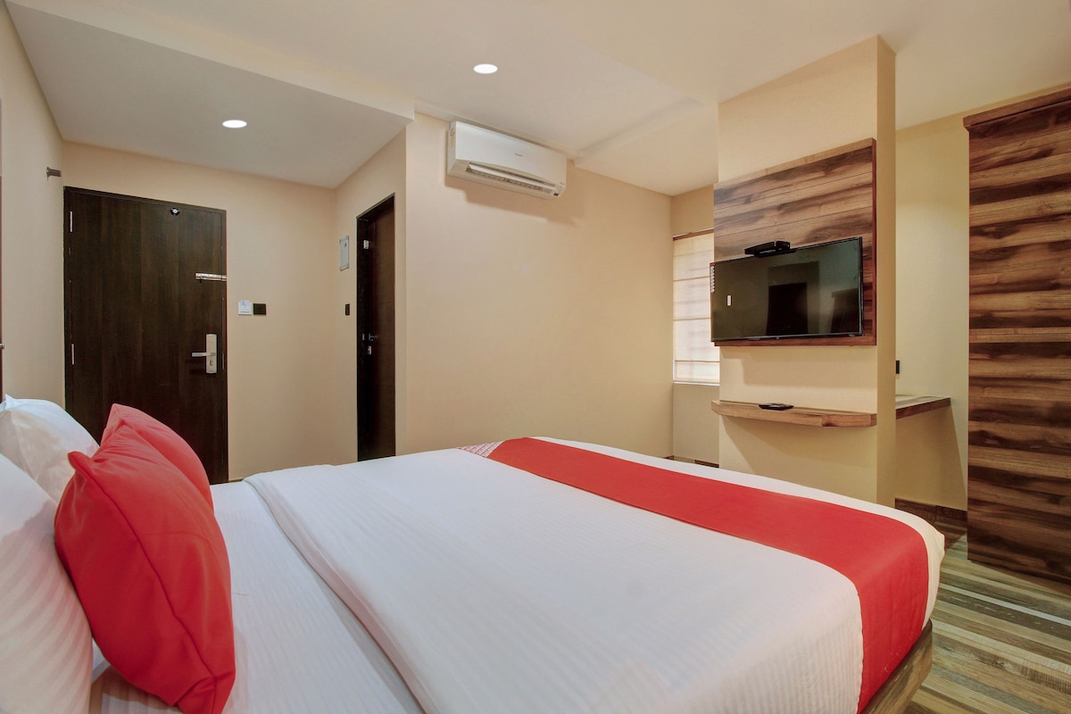 A hotel room with a bed, a television mounted on the wall, and an air conditioning unit.