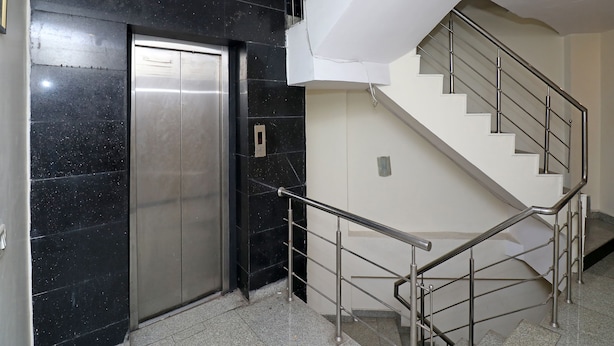 A modern elevator with a digital display, a staircase with metal railings, and a black marble wall.