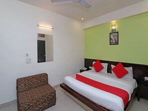 A hotel room with a bed, a chair, a nightstand, a phone, and a wall-mounted light. - OYO 7344 My H Rooms (New Delhi)