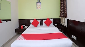 A hotel room with a bed, a nightstand, a mirror, a wall-mounted picture, and a window with curtains.
