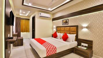 A modern hotel room with a large bed, a bedside table, a TV, and an air conditioning unit.